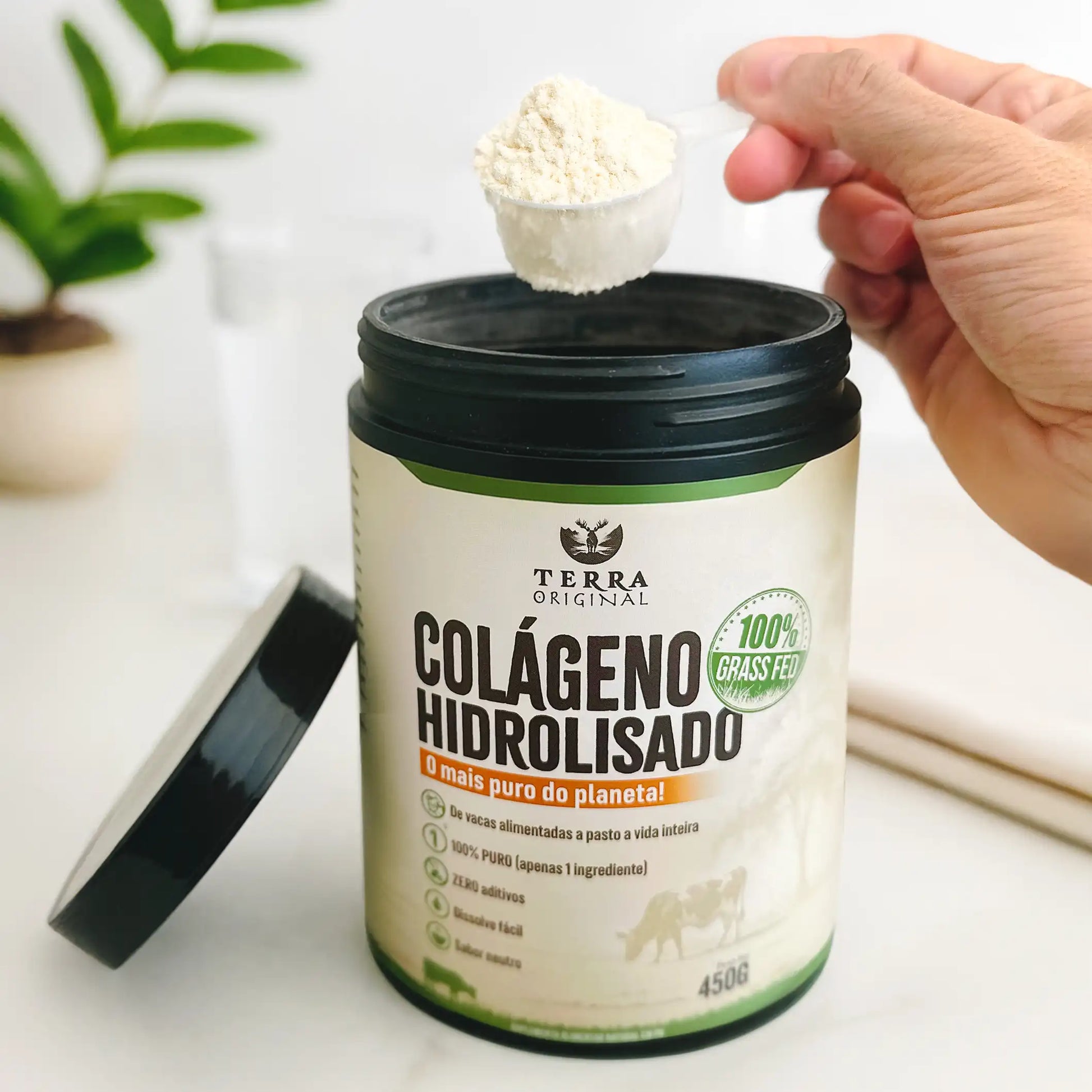 Pote de colágeno hidrolisado 100% puro e grass-fed Terra Original aberto com mão segurando scoop de colágeno em pó