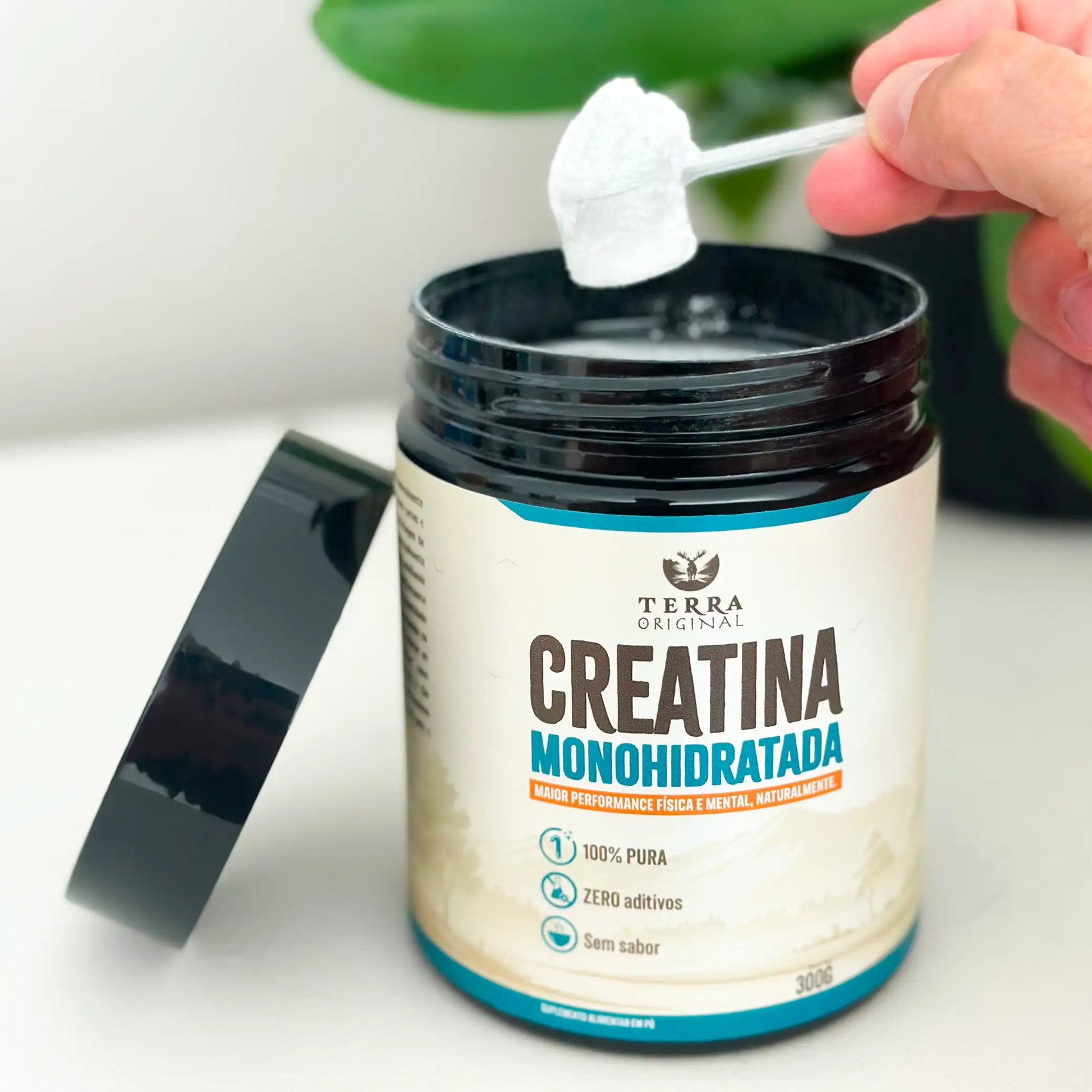 Pote de creatina monohidratada 100% pura e sem aditivos Terra Original aberto com mão segurando scoop de creatina em pó