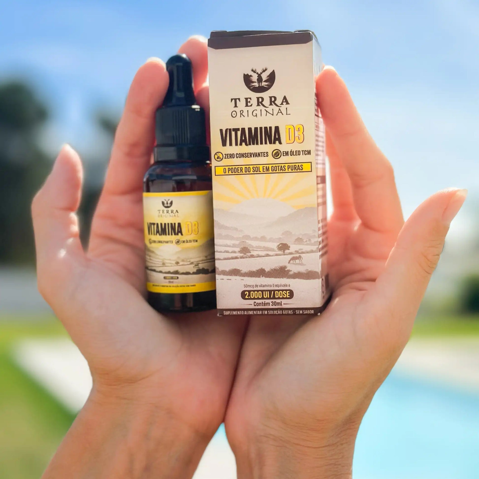 Mãos segurando frasco e caixa de vitamina D3 em óleo TCM Terra Original com fundo externo iluminado