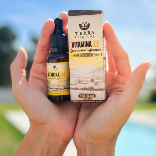 Mãos segurando frasco e caixa de vitamina D3 em óleo TCM Terra Original com fundo externo iluminado